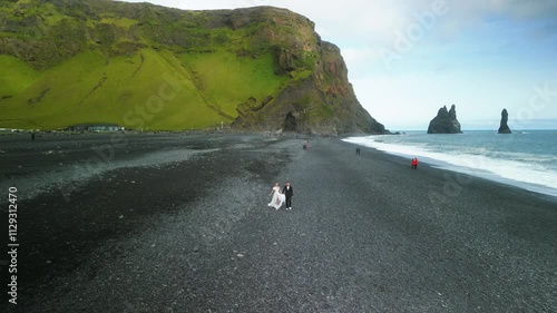 Newlyweds walks along beach holding hands against mountain