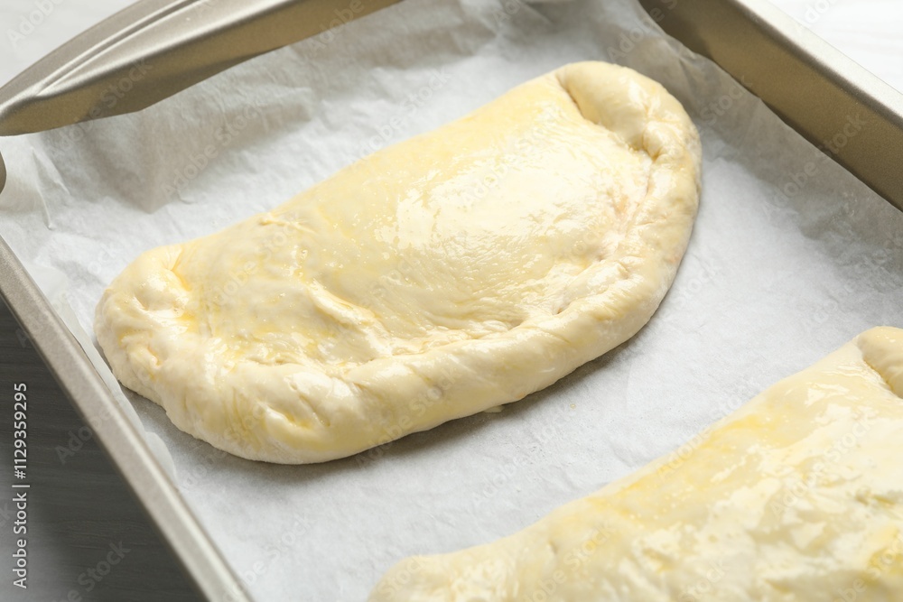 Uncooked calzone pizza in baking dish on white wooden table, closeup Uncooked calzone pizza in baking dish on white wooden table, closeup