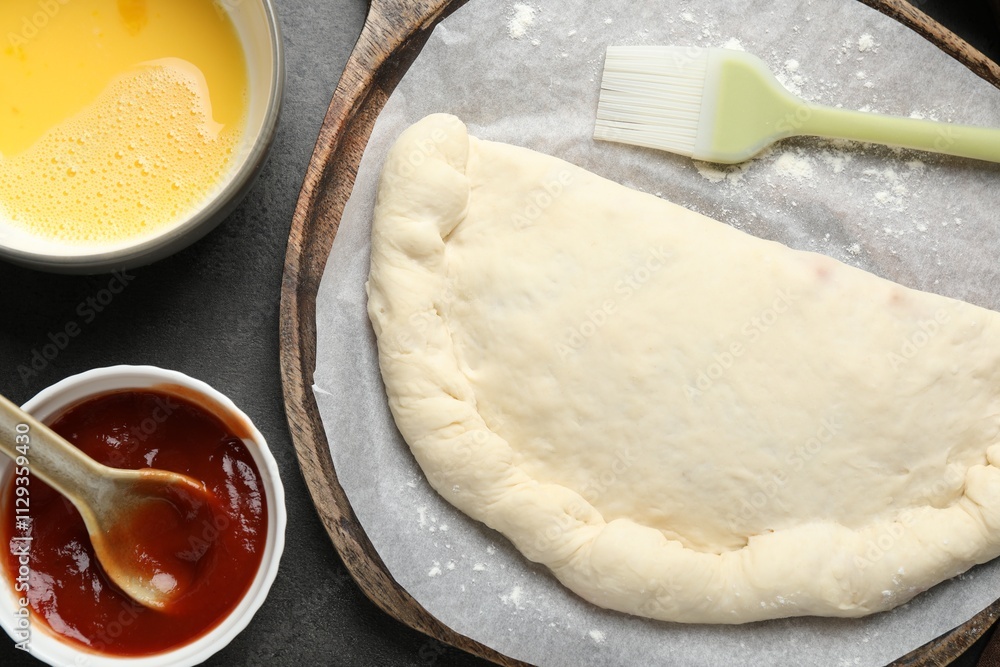 Uncooked calzone pizza, sauce and egg yolk on grey table, flat lay Uncooked calzone pizza, sauce and egg yolk on grey table, flat lay