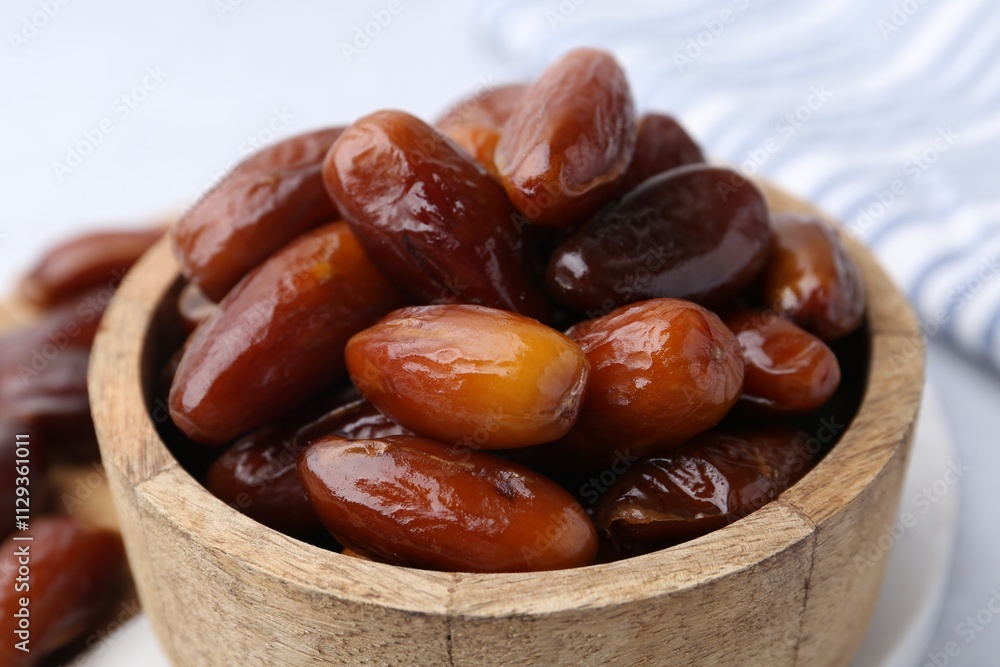Tasty dried dates in wooden bowl on white table, closeup Tasty dried dates in wooden bowl on white table, closeup