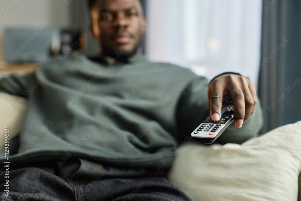 Close up of African American man watching TV at home with focus on hand holding remote, copy space Close up of African American man watching TV at home with focus on hand holding remote, copy space
