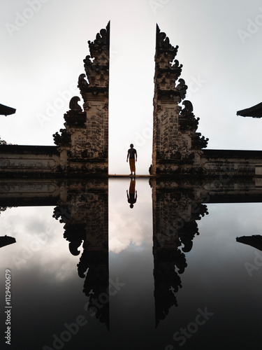 Young man poses with his back to the camera, wearing traditional island clothing in front of the Lempuyang Temple gate during his vacation in Bali