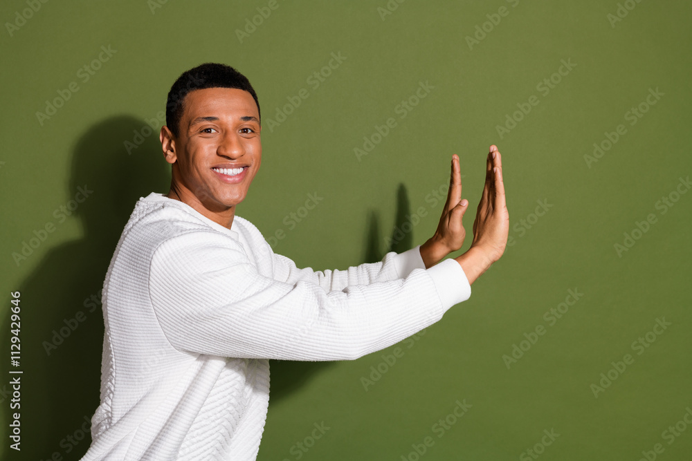 Young man in a stylish white sweater making a playful gesture against a khaki backdrop Young man in a stylish white sweater making a playful gesture against a khaki backdrop