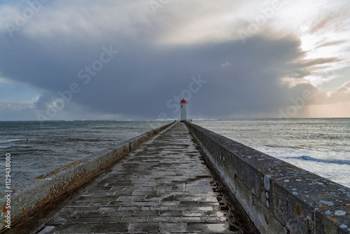 Le phare du Raoulic se profile au bout du môle, sous un ciel nuageux d'automne. Les pavés mouillés du môle serpentent vers lui, ajoutant une touche de caractère à ce paysage maritime. photo