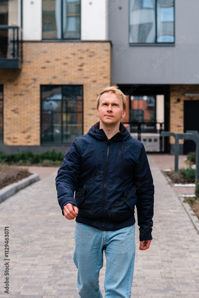A Caucasian man in a jacket walks along the street along the houses A Caucasian man in a jacket walks along the street along the houses