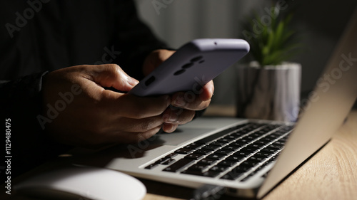 Programmer using smartphone and laptop working at night on cybersecurity project