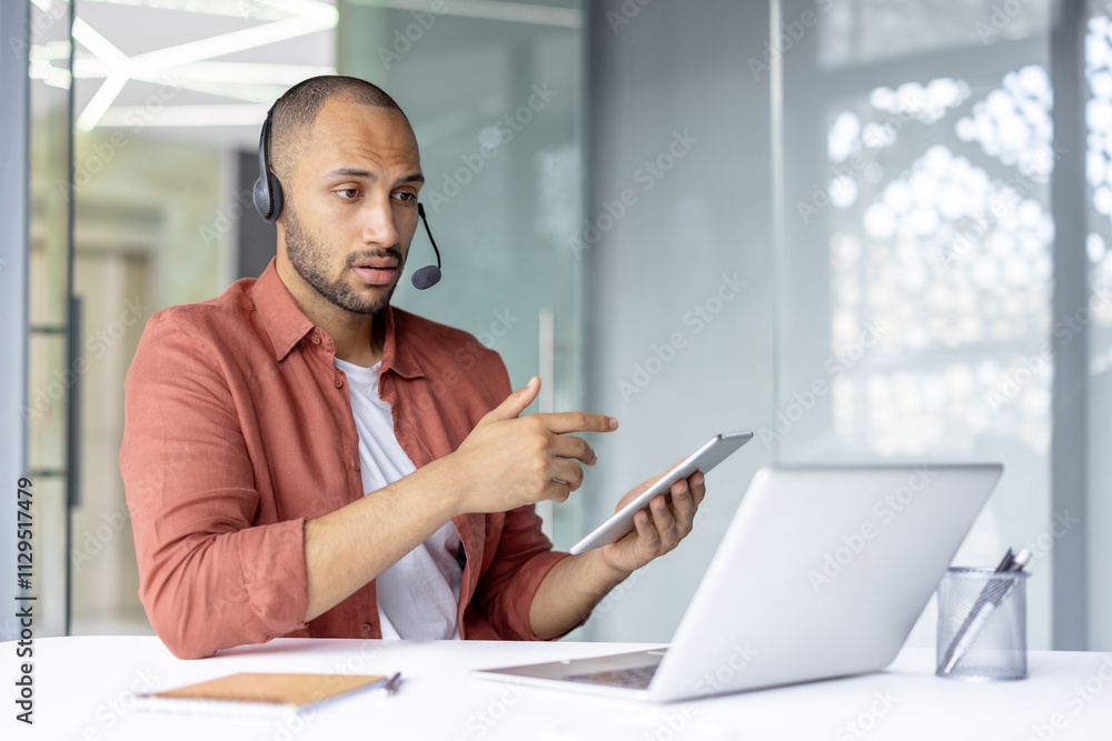 Focused man collaborating online using a tablet, headset, and laptop in a modern workspace. Promotes teamwork, technology, and communication. Focused man collaborating online using a tablet, headset, and laptop in a modern workspace. Promotes teamwork, technology, and communication.
