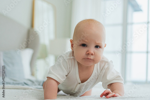 Happy baby. Cute little newborn girl with smiling face crawling on bed in bedroom. Infant baby resting playing lying down on blanket at home. Motherhood happy child childcare concept