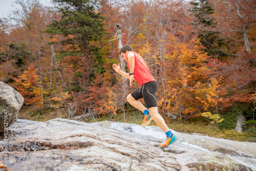 Man running in autumn forest over rocky terrain photo