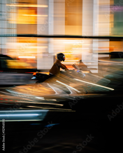 Motorcycle with rider in helmet riding through bright Tokyo city lights at night quickly. Speeding or in a rush amongst traffic and urban buildings with vibrant colours and panning motion blur