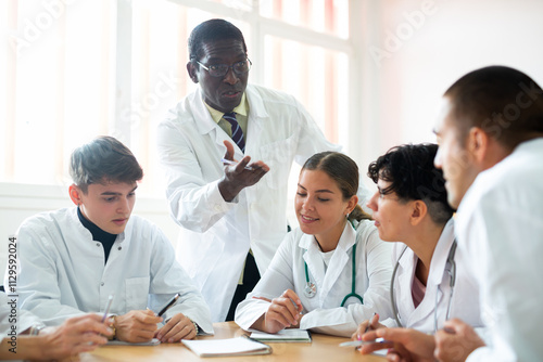 Tableau sur toile African american doctor lecturing to adult audience sitting around same desk during refresher course in university auditorium