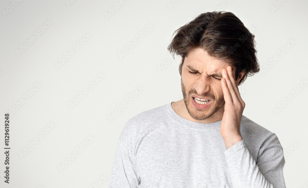 Young beautiful man suffering from headache, isolated on light background Young beautiful man suffering from headache, isolated on light background