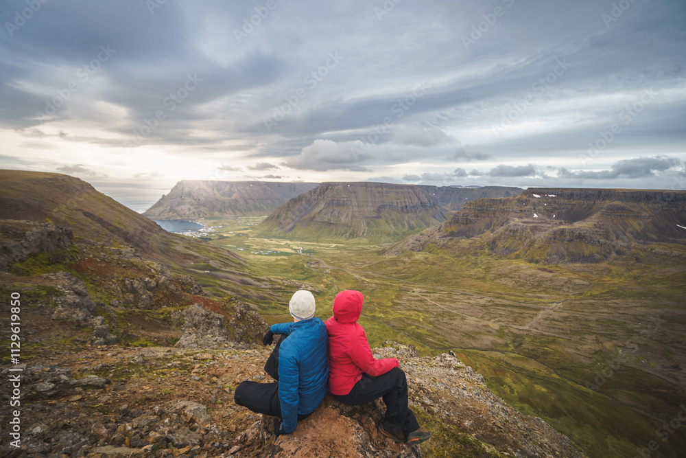 Fototapeta premium A married hiking couple on Bolafjall mountain overlooking Bolungarvik in Iceland’s Westfjords region.