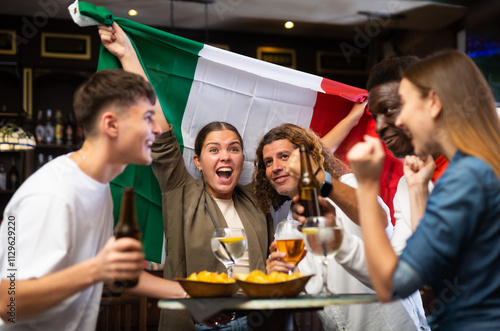 Emotional diverse soccer supporters with flag of Italy celebrating victory of the national team with pint of beer and chips in the pub photo