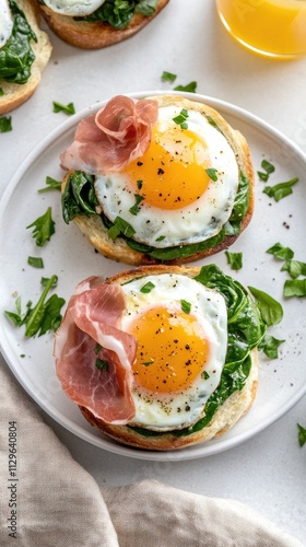 Two soft rolls topped with fresh spinach, ham, and perfectly fried eggs are served alongside glasses of orange juice in a cozy breakfast setting