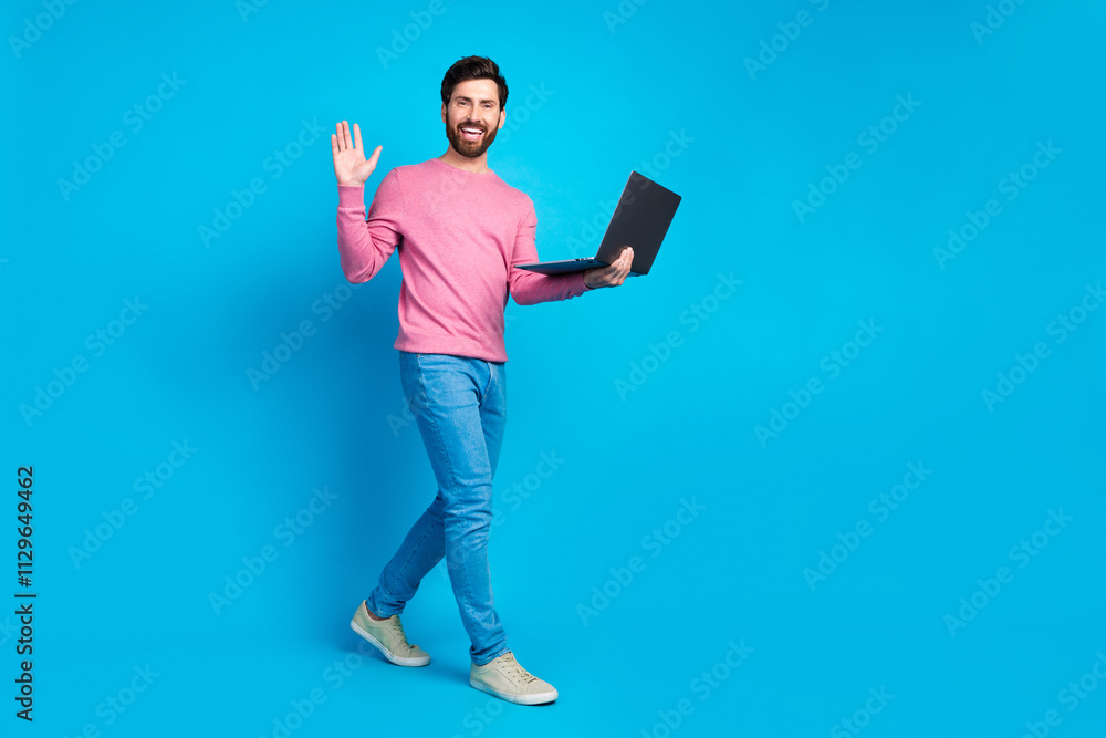Friendly man with beard in casual fashion holding laptop and waving against a vibrant blue background Friendly man with beard in casual fashion holding laptop and waving against a vibrant blue background