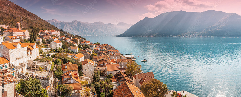 Orange rooftops of Perast village blend with the tranquil blue waters of the bay of Kotor, nestled amidst Montenegro breathtaking mountains at sunset