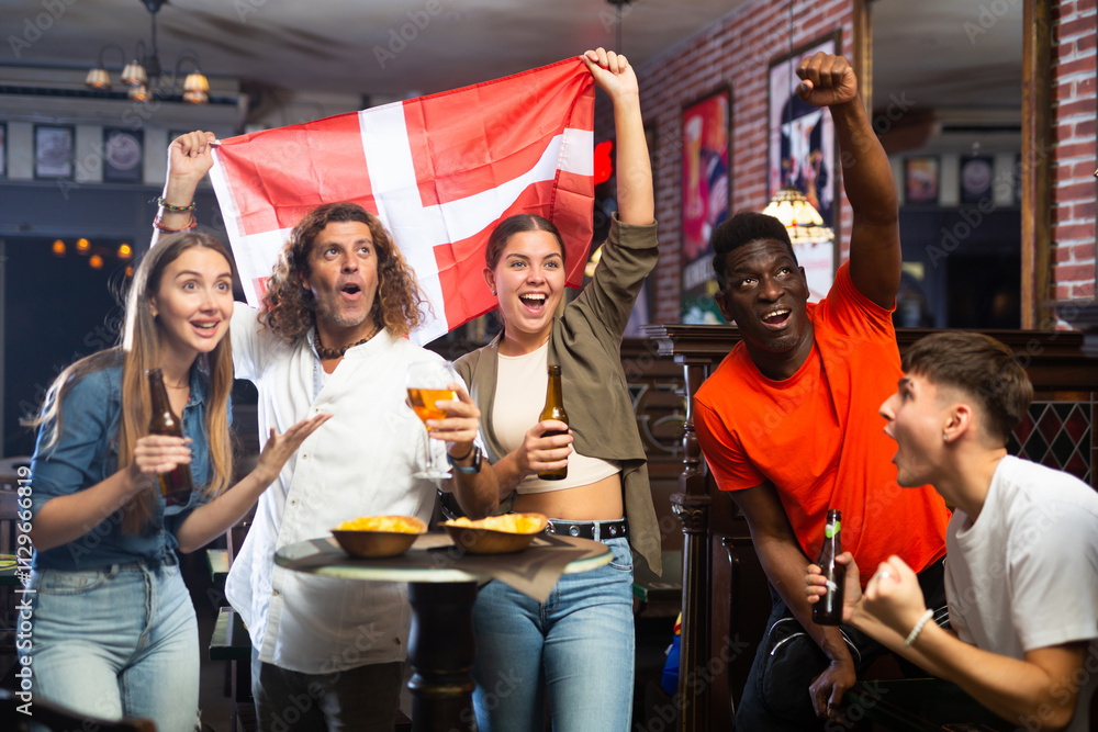 Obraz premium Group of Denmark football team fans spending time in bar, drinking bear and having fun. People with state flag in pub.