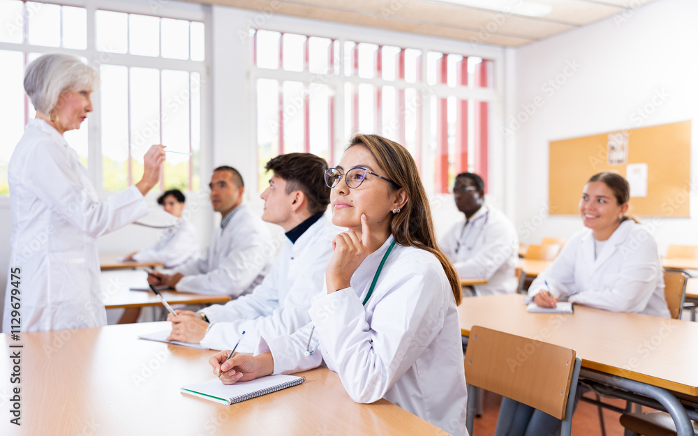 Doctors different age sitting at desk in classroom working during lesson at adult education class Doctors different age sitting at desk in classroom working during lesson at adult education class