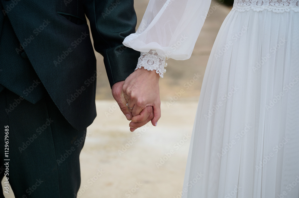 Close-up of a couple holding hands in wedding attire Close-up of a couple holding hands in wedding attire