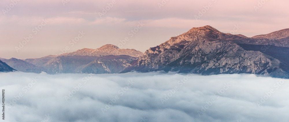 Stunning panoramic view of mountain peaks rising above a thick layer of clouds during a vibrant sunset, creating a breathtaking natural spectacle