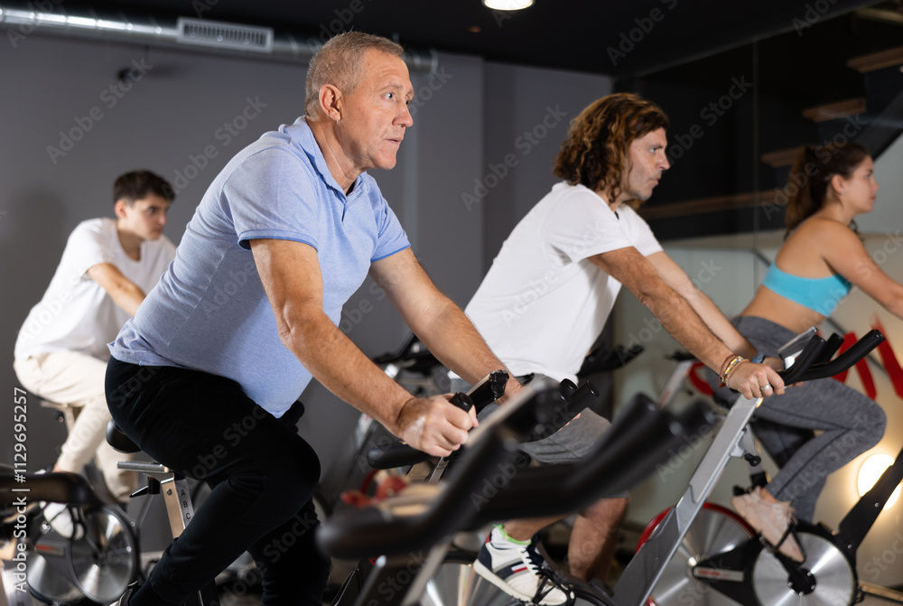 Obraz premium Focused aged man leading healthy active lifestyle doing cardio workout on exercise bike in gym