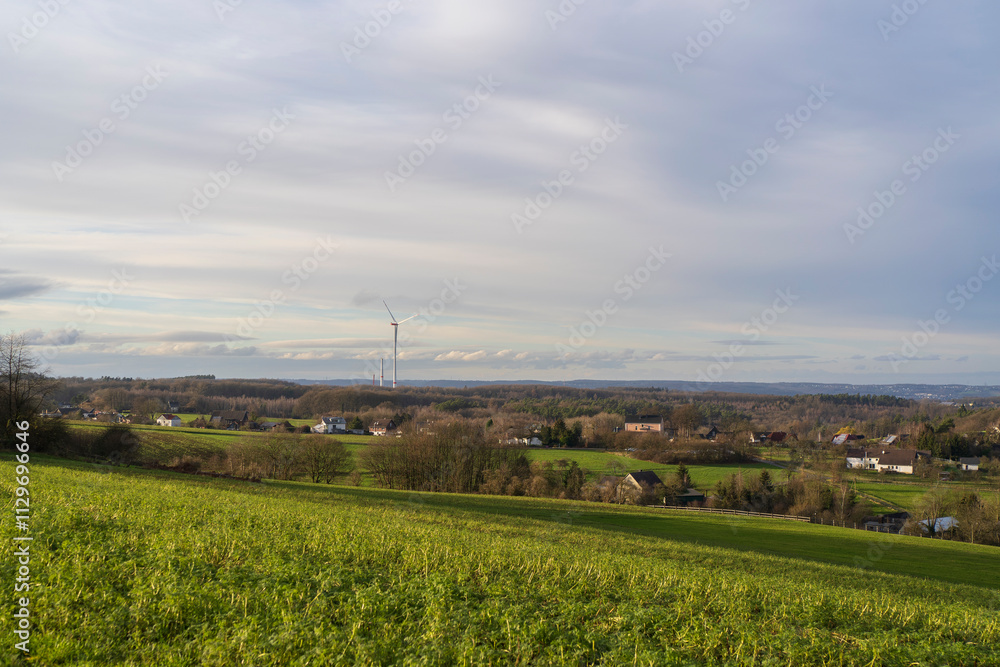 A lone wind turbine next to a tree in a rural German landscape in North Rhine Westphalia. Renewable energy concept A lone wind turbine next to a tree in a rural German landscape in North Rhine Westphalia. Renewable energy concept