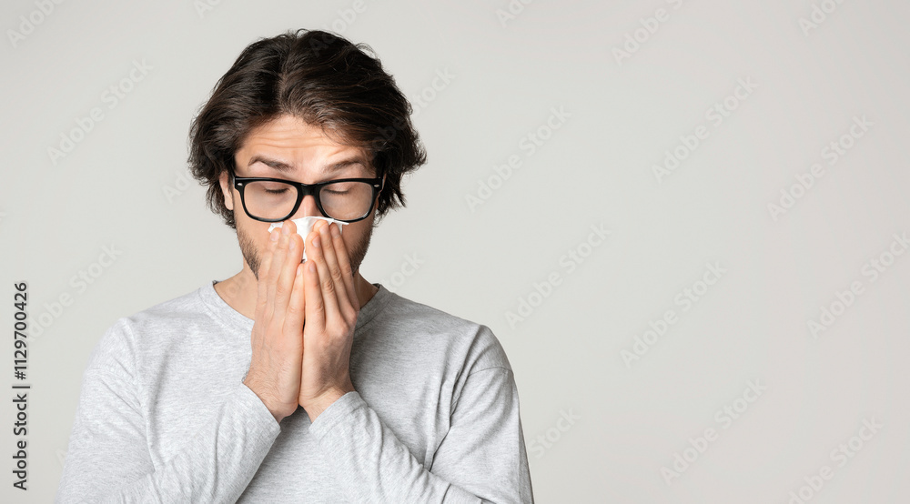 Runny nose and allergy concept. Guy in glasses wipes nose with napkins Runny nose and allergy concept. Guy in glasses wipes nose with napkins