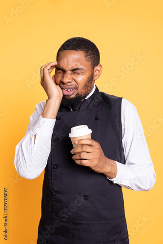 Restaurant worker suffering from a painful migraine while he serves people, drinking a cup of coffee to stay awake. Unwell butler feeling sick with a headache, burnout and fatigue. photo