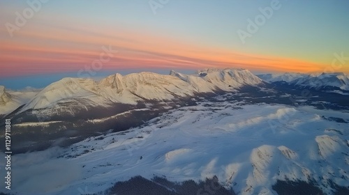 Breathtaking aerial view of snow-capped mountains at sunset.  Pink and orange hues paint the sky above a winter wonderland. photo