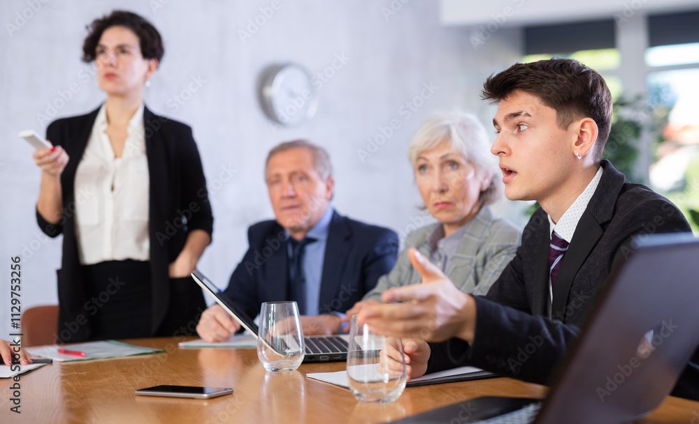 Interested young businessman attending business negotiations at meeting in office asking questions during presentation of partners Interested young businessman attending business negotiations at meeting in office asking questions during presentation of partners