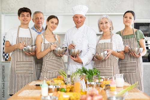 Positive students of culinary classes and cooking instructor posing in kitchen while mixing sauce in metal bowl photo