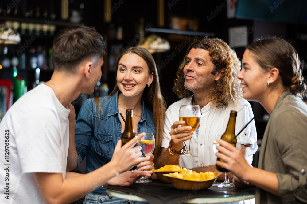 Company of joyful friends drinking beer, eating chips and talking with each other in the sport pub Company of joyful friends drinking beer, eating chips and talking with each other in the sport pub
