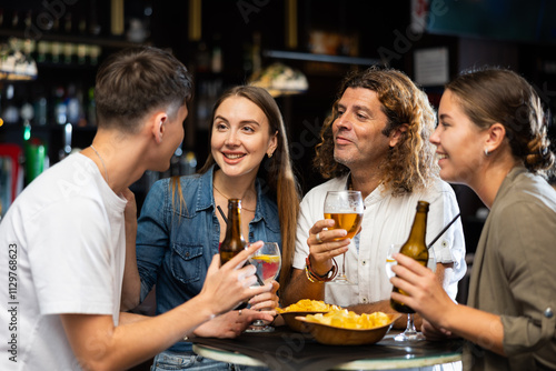 Company of joyful friends drinking beer, eating chips and talking with each other in the sport pub