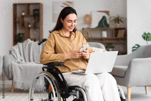 Fotografía Young woman in wheelchair using laptop and mobile phone at home
