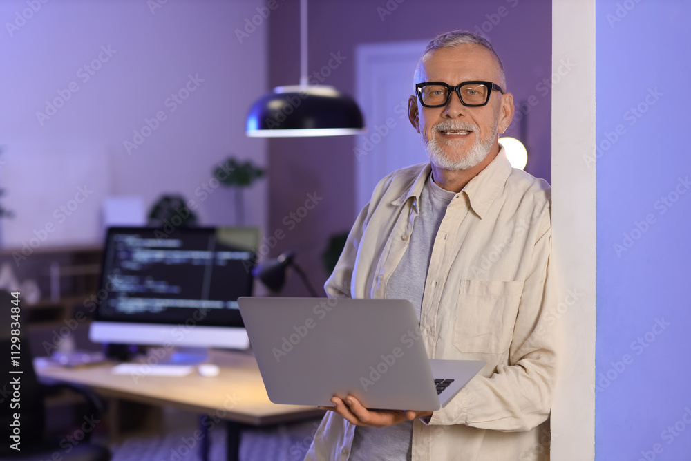 Mature programmer working with laptop in office at night
