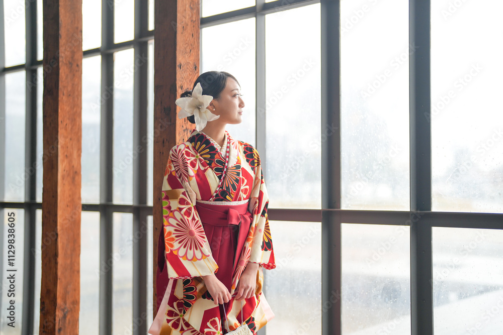 A Japanese woman in her 20s, wearing a red kimono (Hakama), a staple of Japanese university graduates, stands in a clean glass room, looking a little lonely. A Japanese woman in her 20s, wearing a red kimono (Hakama), a staple of Japanese university graduates, stands in a clean glass room, looking a little lonely.
