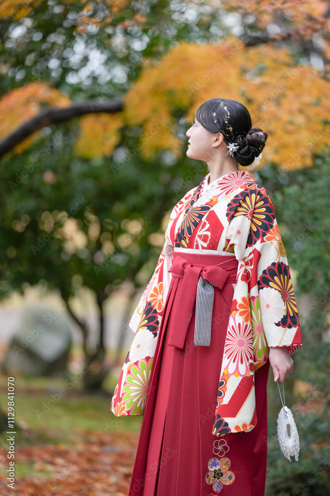 A Japanese woman in her 20s wearing a red kimono (Hakama), a staple of Japanese university graduates, stands in a traditional Japanese park with beautiful autumn leaves. A Japanese woman in her 20s wearing a red kimono (Hakama), a staple of Japanese university graduates, stands in a traditional Japanese park with beautiful autumn leaves.