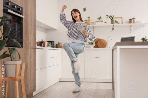 Happy young woman with dollar banknotes in kitchen