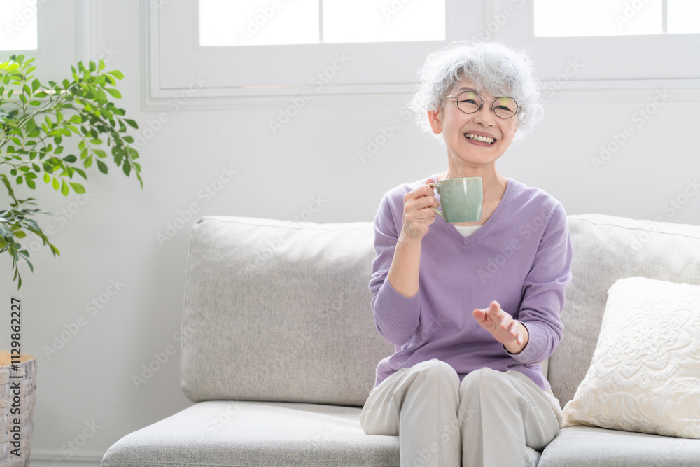 ソファーでコーヒーを飲みながらくつろぐシニア女性 ソファーでコーヒーを飲みながらくつろぐシニア女性