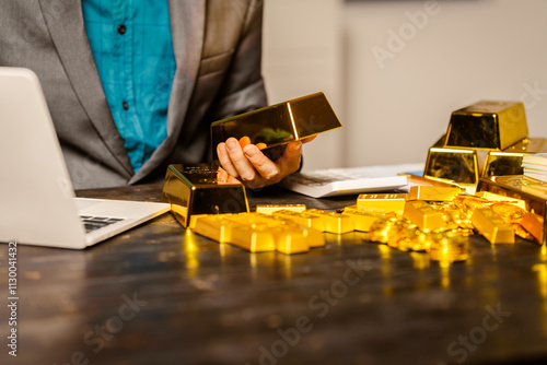 A businessman sits at his desk in a nighttime office, using a laptop to analyze gold bar prices,exchange rates, and investment plans in gold trading, mining,and the stock market amid price increases photo