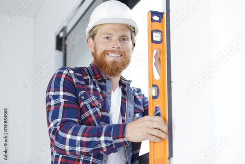 smiling handyman holding spirit level against a wall photo