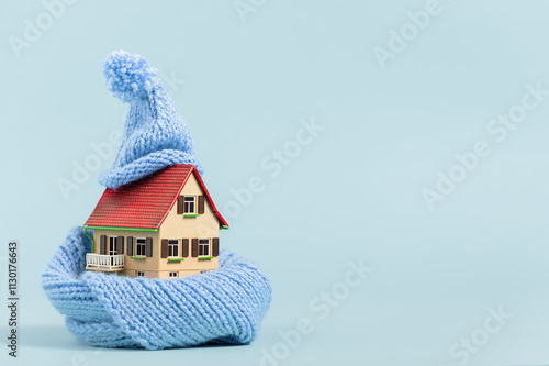 thermal insulation of buildings: old miniature model house with scarf and bobble hat, blue background