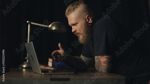 Excited businessman talking by video conference with employees aggressively. Stylish bearded man with tattooed arms gesticulating actively and shouting to web camera of laptop, strict boss, threaten
