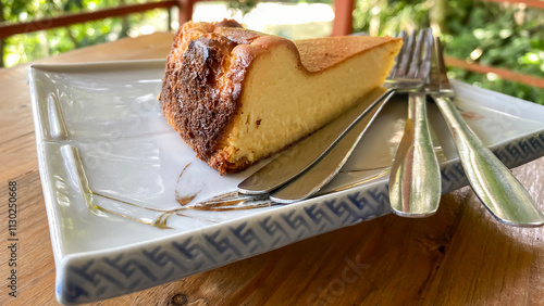 piece of cheesecake on a plate with forks on a wooden tabletop