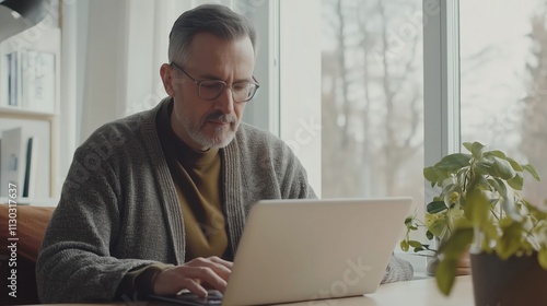 Focused professor working on laptop at home office: researching and typing on computer