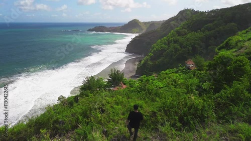 Aerial drone view of a man walking at the coastline with hills and trees, as well as view of coral cliffs and sea with waves from the sea in Surumanis Beach Kebumen Central Java Indonesia photo