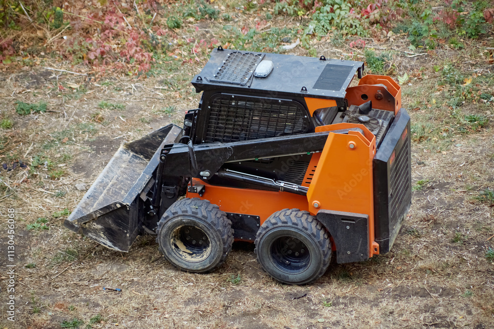 Fototapeta premium Mini loader on an earthen site with dry grass, loader ready to work