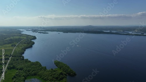 Lower Lough Erne, County Fermanagh, Northern Ireland, June 2023. Drone pushes across the lake in a sweeping vista above the blue water with a moter boat headed west surrounded by green countryside. photo