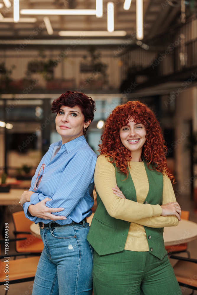 Two confident businesswomen posing with arms crossed in modern office Two confident businesswomen posing with arms crossed in modern office